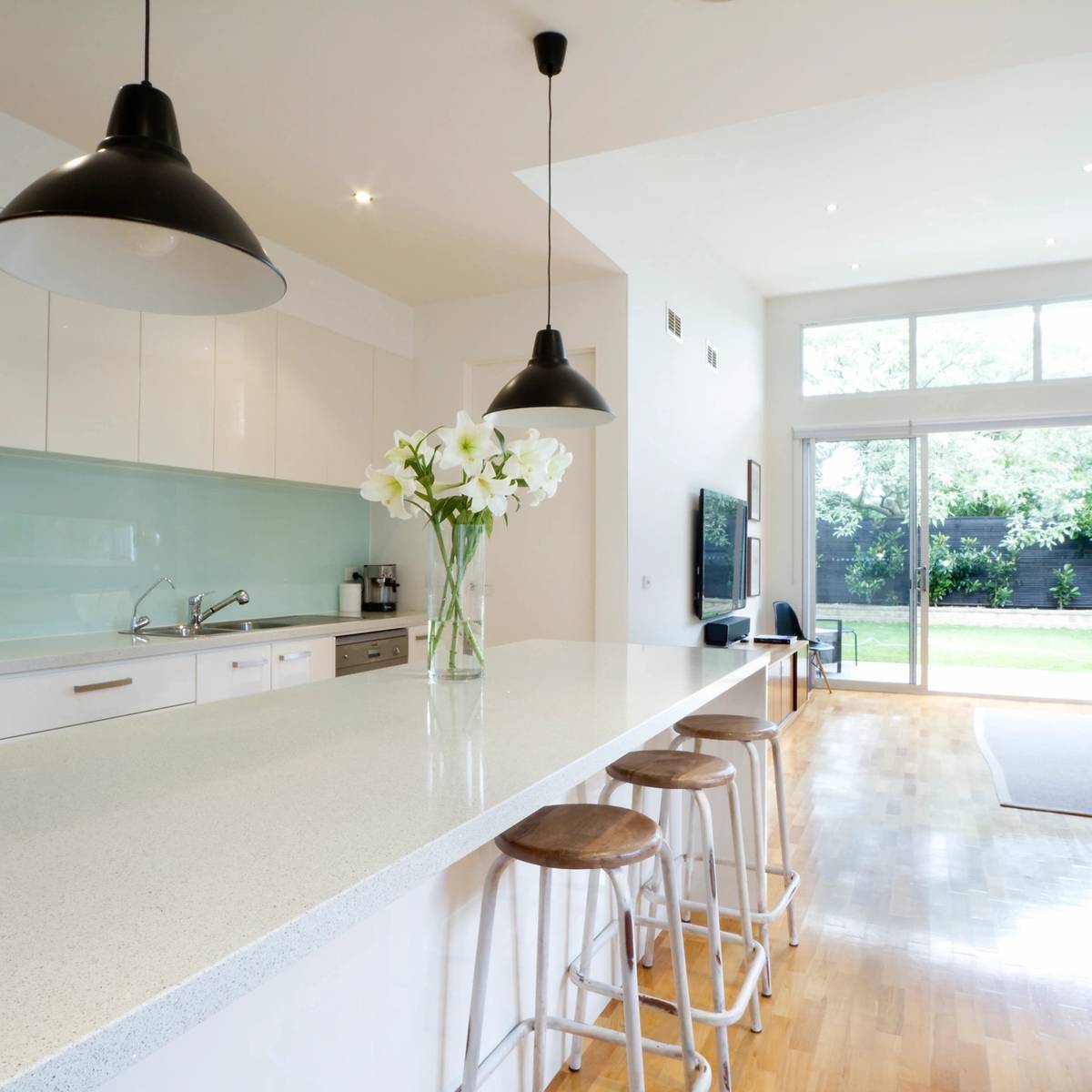 A kitchen with white counters and black pendants.